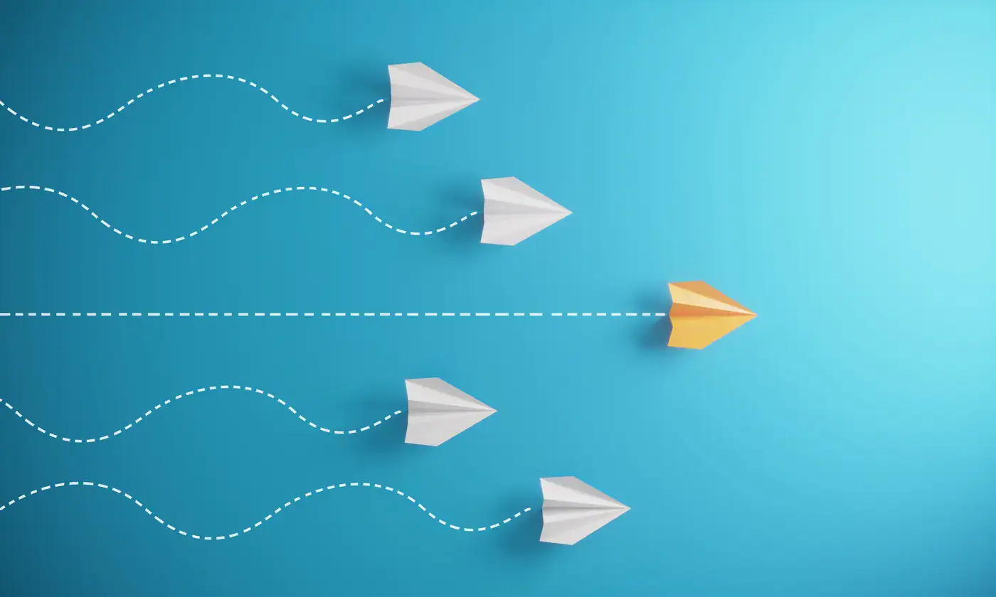 A gold paper plane breaking away from a row of white paper planes onto a direct path